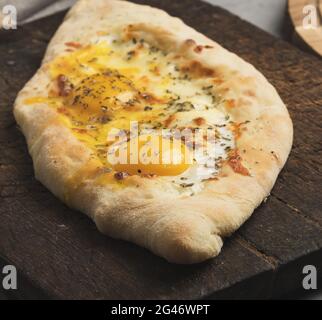 Gebackene Adjarian-Khachapuri mit dem ganzen Eigelb auf Holzbrett, traditionelles Gericht Stockfoto