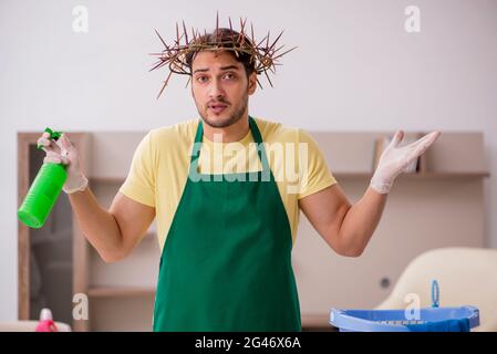 Junger männlicher Auftragnehmer, der auf dem Kopf einen stacheligen Kranz trägt und Hausarbeit leistet Stockfoto