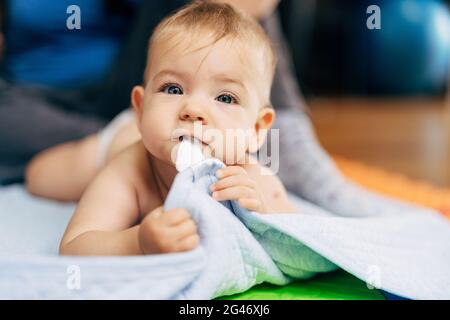 Kleines Baby in Windeln liegt mit seinem Bauch auf einem Blaue Decke und hält den Rand mit seinen Händen und Zähne Stockfoto