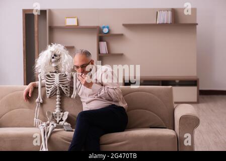 Alter Mann sitzt auf dem Sofa mit dem weiblichen Skelett In unsterbst Liebe Konzept Stockfoto