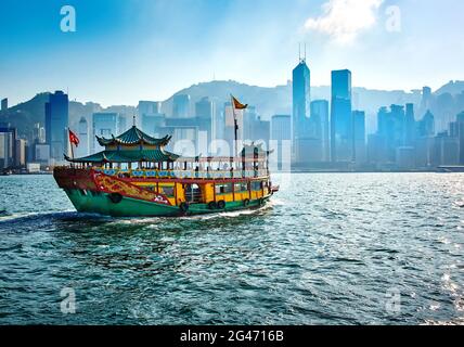 Passagierfähre, die Menschen zwischen den Inseln von Hong Kong mit Wolkenkratzern im Hintergrund transportiert Stockfoto