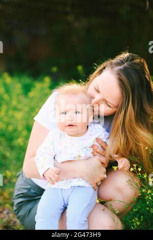 Mutter küsst ihr Baby Mädchen, während sie auf der sitzt Rasen Stockfoto