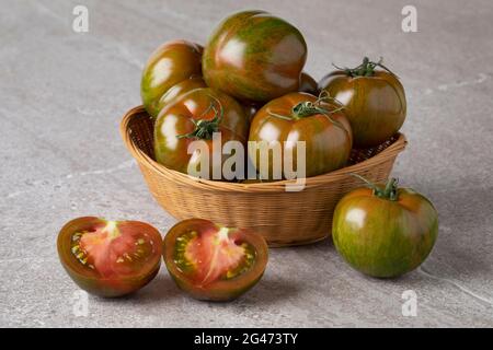 Korb mit reifen roten und grün gestreiften ganzen und halb frischen Tomaten aus der Nähe Stockfoto