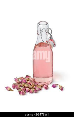 Aromatisches Rosenblütler-Wasser in einer Glasflasche mit getrockneten Rosenblüten vorne isoliert auf weißem Hintergrund Stockfoto