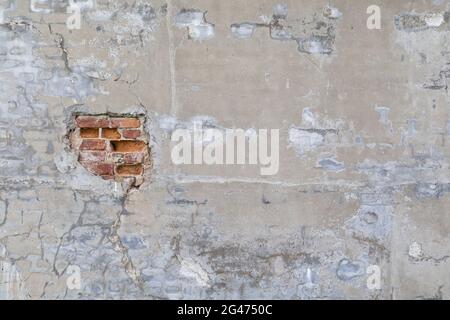 Vorderansicht einer alten, schmutzigen, beschädigten und verputzten Wand. Der Putz ist teilweise abgeschält und zeigt alte Ziegelsteine. Strukturierter Hintergrund im Vollformat. Stockfoto