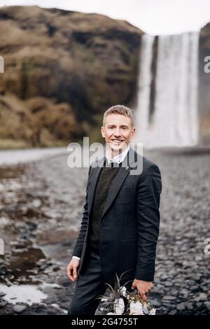 Reiseziel Island Hochzeit. Porträt eines Bräutigams in einer Wolljacke und eines Pullovers in Rauten, der einen Brautstrauß in seinem han hält Stockfoto