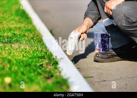 Ein Arbeiter in Overalls malt an einem Sommertag eine Grenze mit weißer Farbe. Städtische Dienstleistungen, Landschaftsbau. Stockfoto