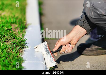 Ein Arbeiter in Overalls malt an einem Sommertag eine Grenze mit weißer Farbe. Städtische Dienstleistungen, Landschaftsbau. Stockfoto