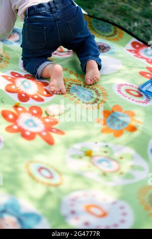 Das kleine Mädchen kriecht auf einer farbigen Decke. Nahaufnahme Stockfoto