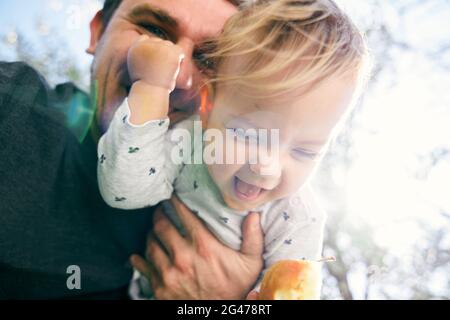 Lächelnder Vater hält ein lachendes Kind mit einer Birne in der Hand vor sich. Nahaufnahme. Niedriger Winkel Stockfoto