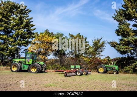 8430 John Deere 8-Radtraktor mit 32'-Rolle und ein 4320-John Deere-Traktor mit 8300-Grain-Bohrer auf einem landwirtschaftlichen Feld. Stockfoto
