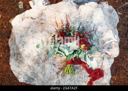 Brautstrauß aus burgunderroten Pfingstrosen, roten Rosen, Eukalyptus-Ästen, Eryngium, Babyatmung, celosia und rote Bänder auf den s Stockfoto