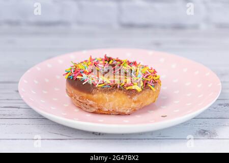 Gebäck-Konzept. Donuts mit Schokoladenglasur mit bunten Streuseln, auf einem rosafarbenen Teller. Draufsicht Stockfoto