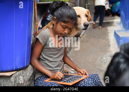 Bengaluru, Indien. Juni 2021. Ein Hund sitzt neben einem Mädchen, das in einem Slum das Alphabet auf einem Schiefer übt, während die Schulen wegen der laufenden Pandemie geschlossen werden. (Foto von Meghana Sastry/SOPA Images/Sipa USA) Quelle: SIPA USA/Alamy Live News Stockfoto