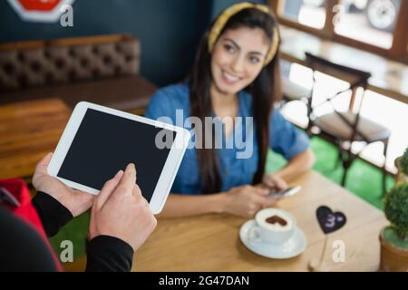 Zugeschnittenes Bild des Besitzers, der das Tablet hält, während der Kunde am Tisch sitzt Stockfoto