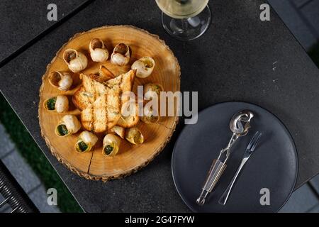Gebackene Schnecken mit Knoblauchöl und Kräutern auf einem Holzbrett Stockfoto