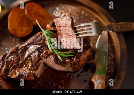 Mittelselten Steak auf Knochen Kalbsrippe mit Kartoffeln auf einem Holzteller Stockfoto