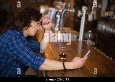 Deprimierter junger Mann, der im Pub ein Handy benutzt Stockfoto