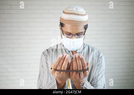 muslimischer Mann mit Gesichtsmaske hält während des ramadan Hand in Gebetsgesten, Stockfoto