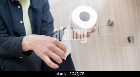 Nahaufnahme der Hand einer Person, die ein Toilettenpapier nimmt Stockfoto