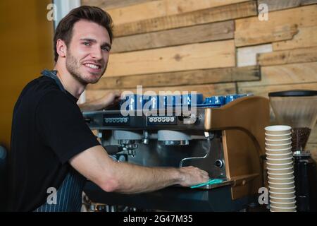 Porträt eines lächelnden Kellners, der die Kaffeemaschine an der Theke putzte Stockfoto