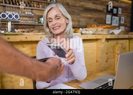 Ältere Frau, die über NFC-Technologie auf dem Mobiltelefon bezahlt Stockfoto