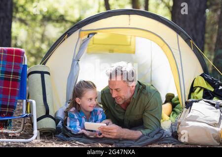 Vater und Tochter nutzen das Handy, während sie sich im Zelt entspannen Stockfoto