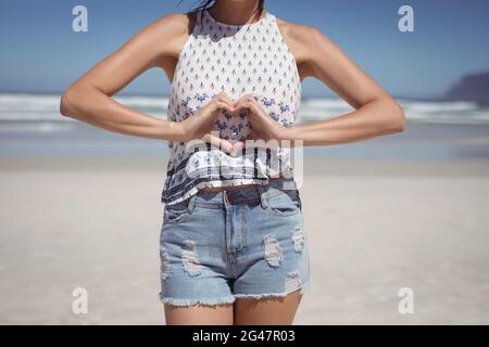 Den mittleren Abschnitt der Frau, die Herzform mit Händen am Strand Stockfoto