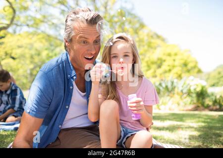 Vater und Tochter blasen Blase mit Bubble Zauberstab auf Picknick im Park Stockfoto