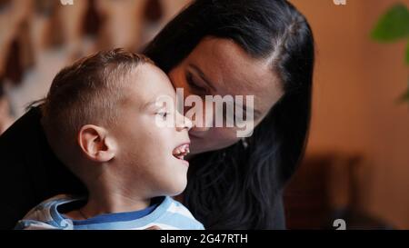 Nahaufnahme Porträt eines kleinen Jungen mit besonderen Bedürfnissen und Mutter lachen an einem Tisch in einem Café, Lifestyle. Die Liebe der Mutter zu ihrem Kind, Inklusion.Happy disab Stockfoto