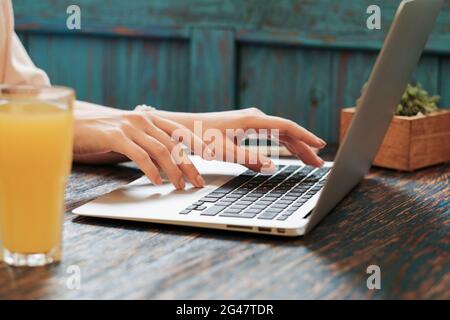 Nahaufnahme einer nicht erkennbaren Frau, die ihren Laptop für ihre Fernarbeit benutzt, während sie im Restaurant sitzt, und einer freiberuflichen Tänzerin, die online über das Internet arbeitet. Stockfoto