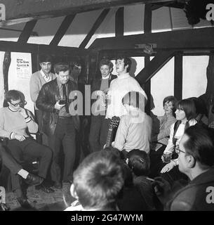 1970, historische Volksmusik, in einem Raum in einem hölzernen, gestrahlten Country Pub, ein Publikum, das einem jungen Mann in einem Wollpullover mit Rollkragen lauscht, sein Pint Besen ausstanzt und ein Lied im Castle Inn, Colchester, Essex, England, Großbritannien, singt. Stockfoto