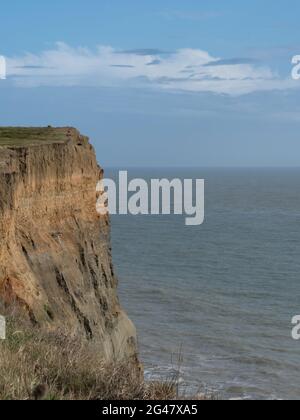 Geschichtete Klippen unter einer kleinen Schicht attraktiver Wolkenwolken am blauen Himmel über dem ruhigen Atlantischen Ozean Stockfoto