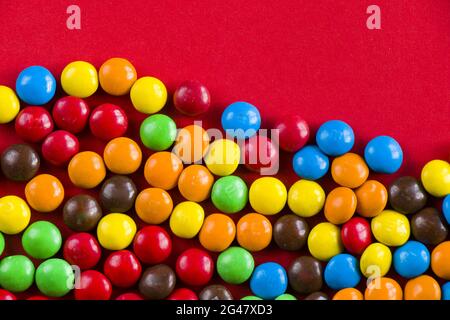 Draufsicht auf eine Gruppe von bunten süßen Bonbons, die auf roter Oberfläche verstreut sind, um Platz für Kopien zu schaffen Stockfoto