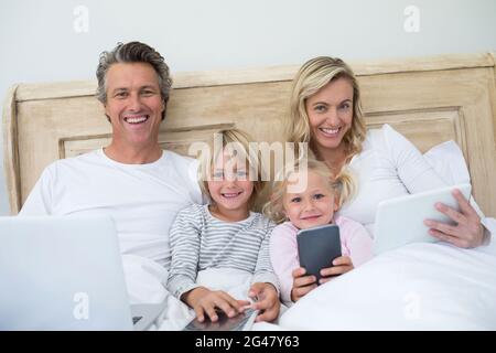 Familie mit digitalem Tablet, Mobiltelefon und Laptop auf dem Bett im Schlafzimmer Stockfoto