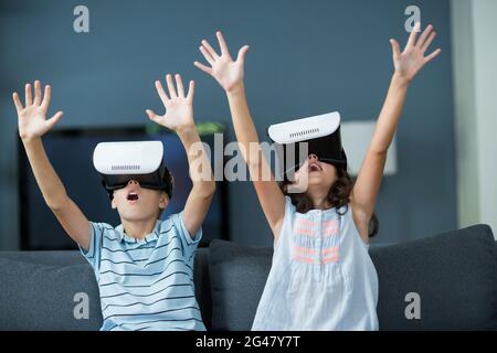 Geschwister, die ein Virtual-Reality-Headset im Wohnzimmer verwenden Stockfoto