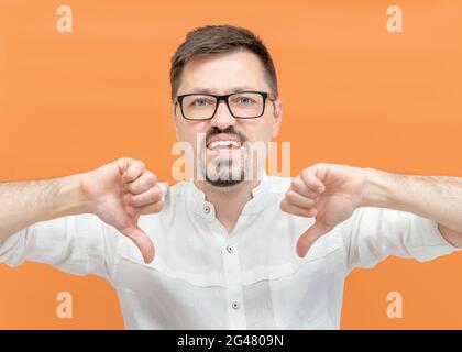 Wütend verärgerten bärtigen Mann in beiläufiger auf gelbem Hintergrund unglücklich zeigt eine Geste der Abneigung mit seinen Händen, zeigt mit zwei Daumen nach unten und schaut auf die Kamera. Negatives Vorzeichen, Ablehnungskonzept. Stockfoto