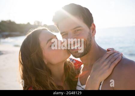 Porträt eines lächelnden Mannes, der von seiner Freundin am Strand geküsst wurde Stockfoto