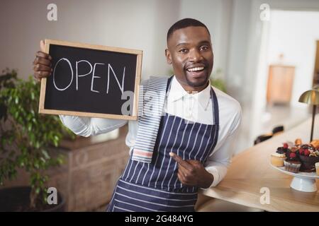 Lächelnd Kellner zeigt Tafel mit Schild "geöffnet" Stockfoto