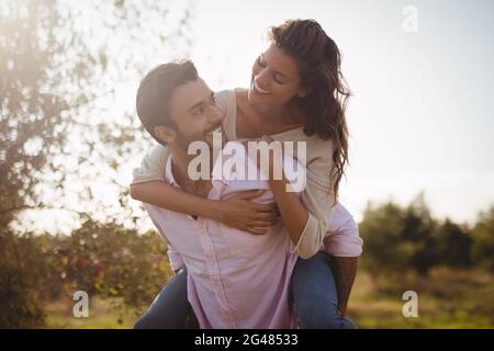 Junger Mann huckepack Frau am Bauernhof während sonniger Tag Stockfoto