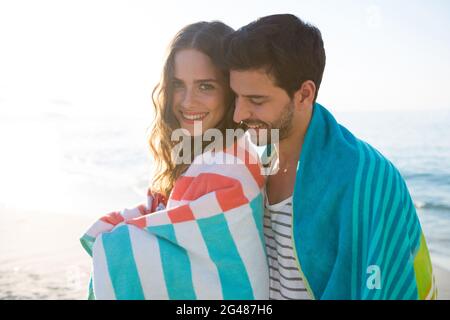 Glückliches junges Paar, das am Strand in eine Decke gehüllt wurde Stockfoto