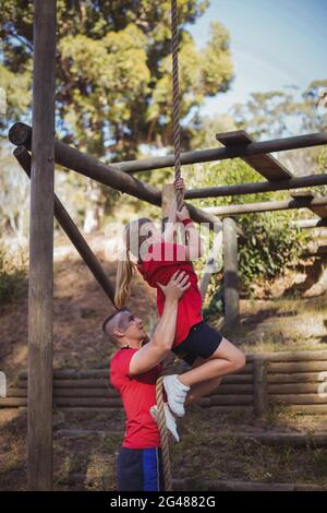 Trainer, der einem Kind beim Klettern an einem Seil im Bootcamp hilft Stockfoto