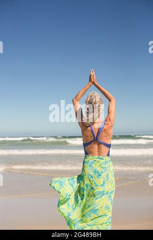 Rückansicht einer Frau, die Yoga praktiziert, während sie gegen das Meer steht Stockfoto