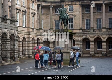 Einige feuchte Touristen auf einem Spaziergang stehen unter der Reiterstatue von Charles II auf dem Parliament Square, Edinburgh, Schottland, Großbritannien. Stockfoto