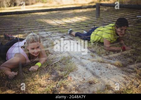 Entschlossene Frauen, die während eines Hindernislaufes unter dem Netz kriechen Stockfoto