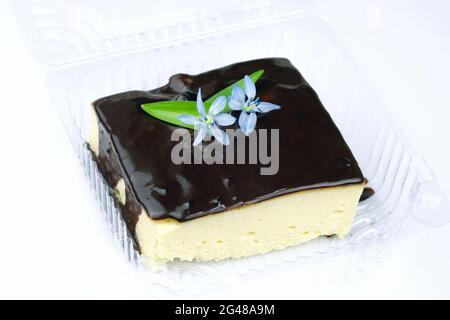 Quark-Auflauf mit Schokolade in einem Plastikbehälter gegossen. Eine Scheibe cremiges Soufflé mit Schokolade, verziert mit einer blauen Blume. Deliciou Stockfoto