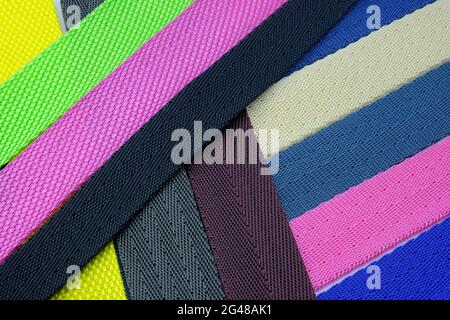 Farbiger Hintergrund von schräg gefalteten Bändern. Farbige Polyester-Gürtel, Musterpalette für die Herstellung von Schultergurten für Taschen und Rucksäcke. Stockfoto