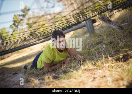 Entschlossene Frau, die während eines Hinderniskurses unter dem Netz kriecht Stockfoto