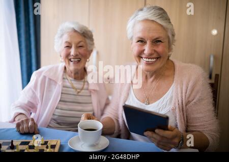 Porträt lächelnder älterer Freunde, die beim Schachspielen Kaffee trinken Stockfoto