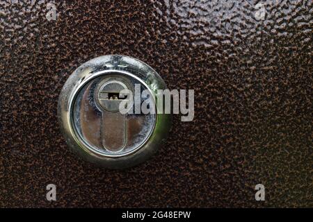 Ein Schlüsselloch an der braunen Tür. Typisches Türschloss. Ein metallisches Schlüsselloch an einer Metalltür. Mit Schlüsselloch-Detail. Stockfoto